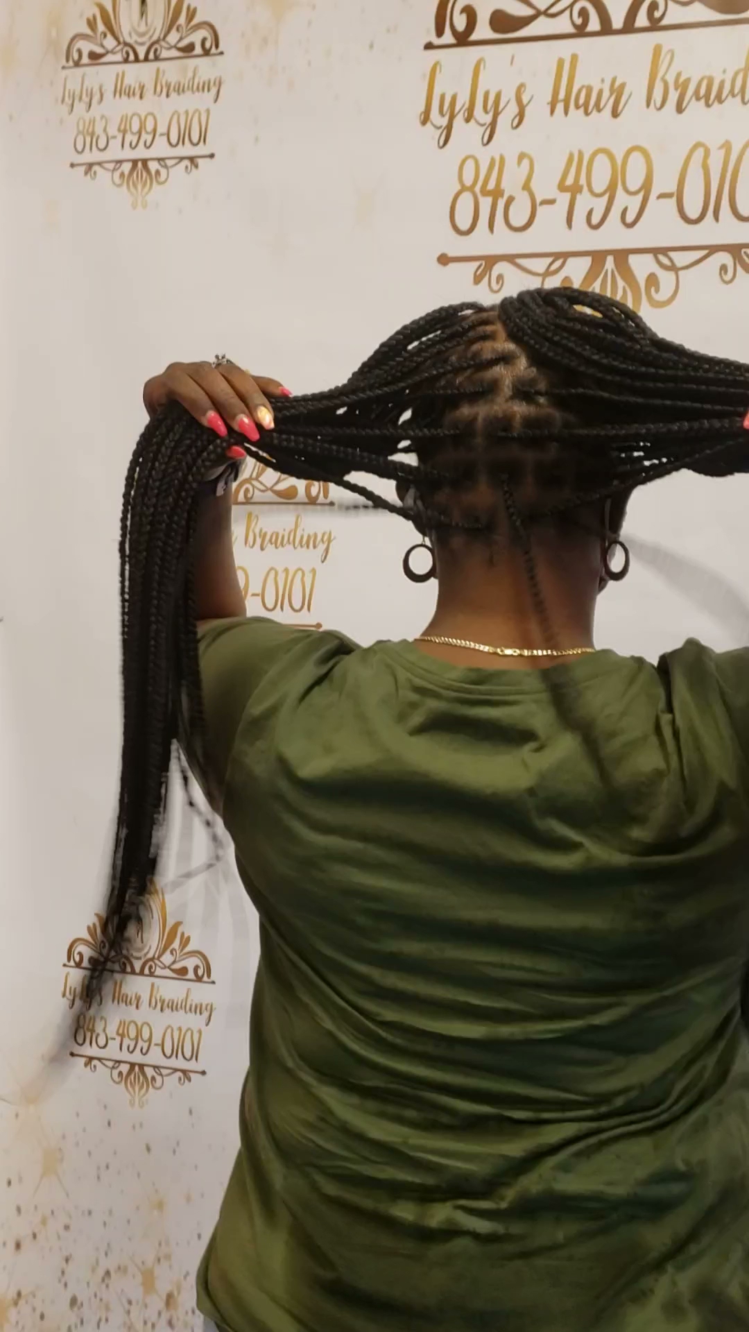 A client with long braids in front of the salon backdrop